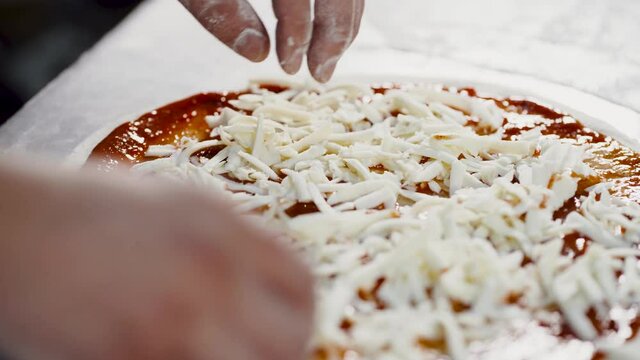 Close-up of a chef pouring cheese on a traditional Italian Pizza's Restaurant pizza.
