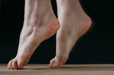 Close up low key  of bare foot dancer lifting on tip toes, on black background