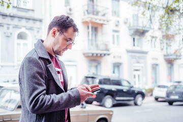 Young urban professional man using smartphone. Businessman holding mobile smartphone using app texting sms message