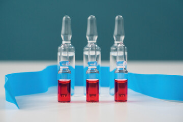 A row of red and transparent vials with medicine on a blue background are on the table. Horizontal composition. Foreground.