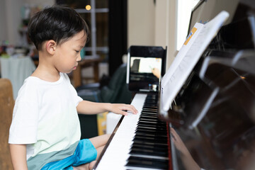 A boy is studying piano online with tablet.