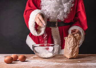 Santa Claus hands sprinkle flour, preparation for dough. Red santa's clothes and white beard on black background.
