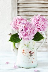 pink hydrangeas in a vintage coffee pot against a background of rough plaster and blinds. style of Provence. copy space. place for text.