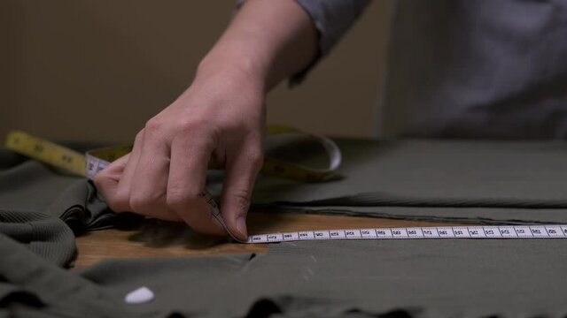 Close up hand of professional seamstress working with grey fabric takes measures use centimetre. Fashion designer in studio designing new collection clothes in sewing workshop concept