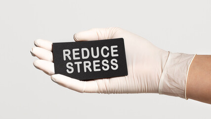 Closeup of the hand in a white sterile glove holding a card with text - REDUCE STRESS