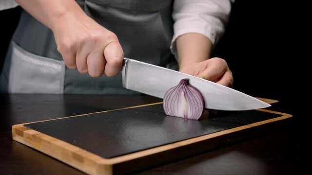 Female hands cutting in slices red onion with knife on cutting board. Close up
