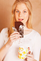 young cute blond girl eating chocolate and drinking coffee close up