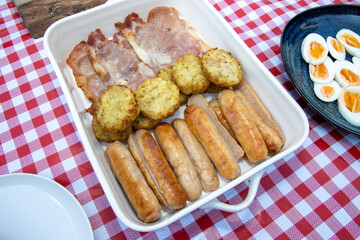 A traditional British breakfast in a baking trey including bacon sausages and hash browns on a breakfast table