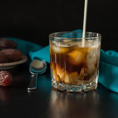 Cold brew iced coffee with a  milk,a tea spoon , a dates  and a  blue napkin on a black background . Summer drink .  