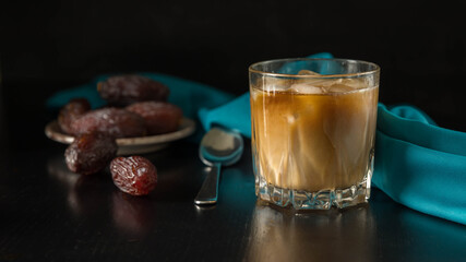 Cold brew iced coffee with a  milk,a tea spoon , a dates  and a  blue napkin on a black background . Summer drink .  