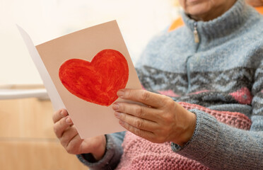Closeup postcard with a heart in the hands of an old woman. Grandmother reads congratulations from...