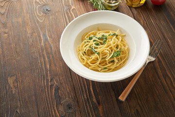 Spaghetti pasta with spinach leaves and cheese on a white plate on the wooden background, top view from above