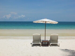 White beach bed with white umbrellas rests on white sand, sea front and blue sky.