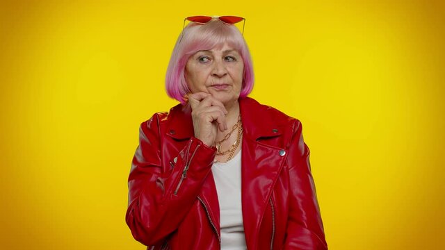 Inspired mature old granny woman with pink hair in red leather jacket pointing finger up with open mouth, showing Eureka gesture creative plan feels excited with good idea. Senior rocker grandmother