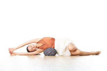 Restorative yoga with a bolster. Young sporty attractive woman in bright white yoga studio, lying on bolster cushion, stretching and relaxing during restorative yoga. Healthy active lifestyle