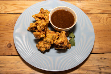 A delicious plate of Indian Pakoras with a spicy nipping sauce on a wooden kitchen table