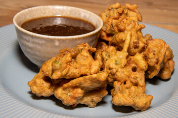 A delicious plate of Indian Pakoras with a spicy nipping sauce on a wooden kitchen table