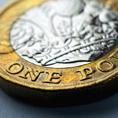 1 one British pound coin. Focus is on denomination of coin and name of currency of UK. Dramatic square illustration with increased contrast and saturation about money and economy of Britain. Macro