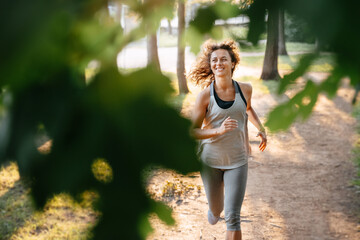 Young red-haired woman runs a marathon outdoors in a city park in the forest. Warm rays of the sun through the branches of the trees.