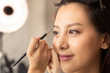 Young asian woman in bedroom. Make-up artist in beauty studio doing makeup for beautiful girl.Beautiful young master make-up artist applies powder brush to face.Woman Profile making up using pencil.