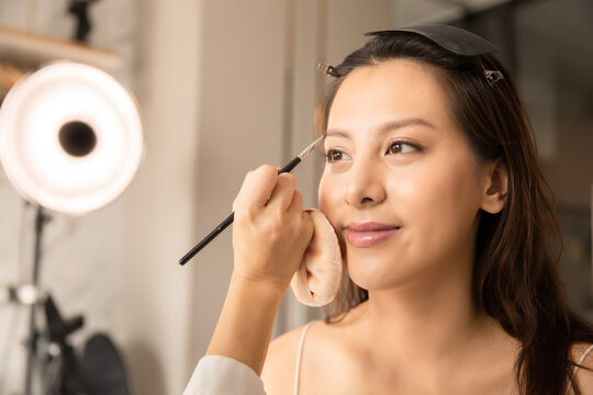 Young asian woman in bedroom. Make-up artist in beauty studio doing makeup for beautiful girl.Beautiful young master make-up artist applies powder brush to face.Woman Profile making up using pencil.