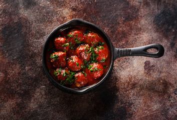 Meatballs in tomato sauce from beef and pork meat with fresh herbs on a cast iron pan. Dark background. Top view.