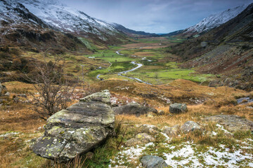Fototapeta premium dramatic photo of the wintry autumn weather and snow capped mountains in the Nant Ffrancon Pass and Ogwen valley in Snowdonia National Park in North Wales.