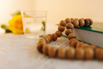 Rosary beads close-up on the Quran against the background of a glass of water during suhoor or iftar on the Ramadan time