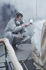 Car painting and automobile repair service. Auto mechanic in white overalls paints car with...