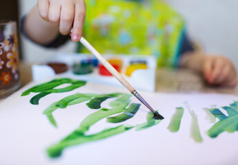 Naklejka premium Top view of the small child is drawing with bright paints on paper, close up.