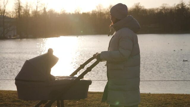 Mother with baby stroller on walk in the park by pond in the evening, mom pushing baby carriage in Catherine Park, Tsarskoye Selo, Pushkin, Saint Petersburg. High quality 4k footage