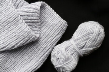 Gray yarn for knitting and a piece of finished product from them on a black background