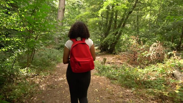 Teenage African American mixed race  girl young woman hiking with red backpack and taking photographs with a camera in forest woodland 
