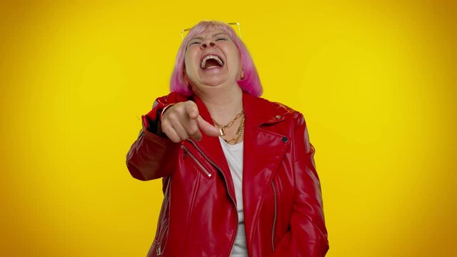 Elderly amused granny woman pointing finger to camera, laughing out loud, taunting making fun of ridiculous appearance funny joke. Senior old grandmother on yellow background. People emotions. Hey you