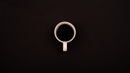 Top view of white ceramic mug with black coffee on black background.