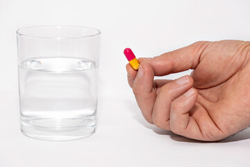 close up of male hands holding pill capsule vitamin supplement with glass of water on white background close up