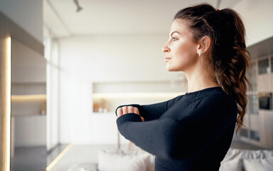 Fototapeta na wymiar Portrait of a confident athletic woman of European appearance doing muscle stretching exercises. Sports morning in the apartment. Healthy lifestyle and proper nutrition.