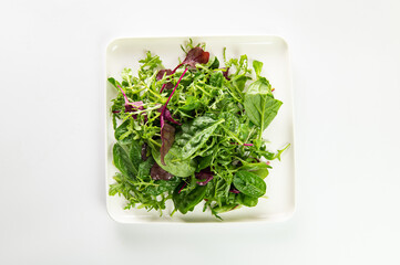 salad mix of fresh herbs, arugula, chard, spinach in a plate on a white plate, top view