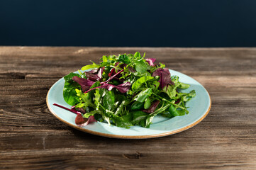 salad mix of fresh herbs, arugula, Swiss chard, spinach in tarenle on a wooden background, top-side...