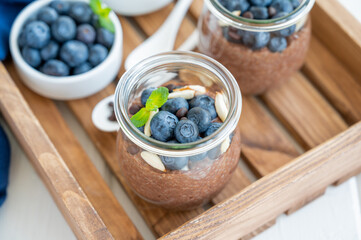 Chocolate chia pudding with blueberry, almonds and mint on top in a glass jar on a white wooden background. Healthy food. Copy space.