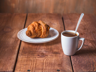 Light breakfast with croissant and black coffee in a white mug
