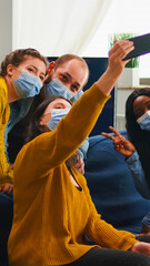 Multiracial friends taking selfie with face masks during covid 19 outbreak, new normal lifestyle concept with people having fun in living room respecting social distance to prevent virus spread