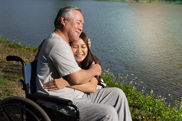 Elderly senior gray-haired man in a wheelchair resting the body with Daughter or granddaughter after receiving medical treatment in the park, Pensioners retirement concept