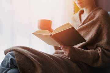 Young woman reading a book and drinking coffee at home - Powered by Adobe