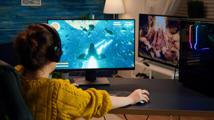 Over the shoulder woman gamer playing online professional shooter game on computer at home late at night. Professional player testing online video games on pc with modern technology network wireless. © DC Studio