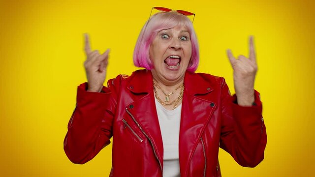 Overjoyed stylish elderly granny woman showing rock n roll gesture by hands, cool sign, shouting yeah with crazy expression, dancing, emotionally rejoicing in success. Senior mature old grandmother