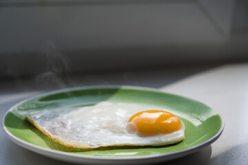 A freshly cooked hot fried egg sits on a green plate. Healthy breakfast. Close-up.