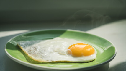 A freshly cooked hot fried egg sits on a green plate. Healthy breakfast. Close-up.