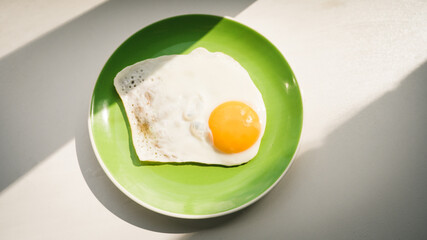 A freshly cooked hot fried egg sits on a green plate. Healthy breakfast. Close-up. View from above.