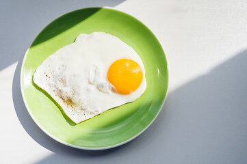 A freshly cooked hot fried egg sits on a green plate. Healthy breakfast. Close-up. View from above.